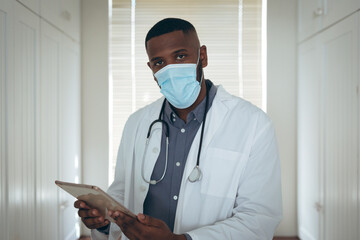 Portrait of african american male doctor wearing face mask using digital tablet