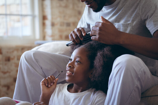 African american man sitting on bed doing his daughter hair