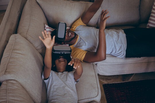 African american man and his daughter lying in living room using vr headset