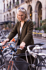 Mature woman chooses rental bike on city street. High quality photo