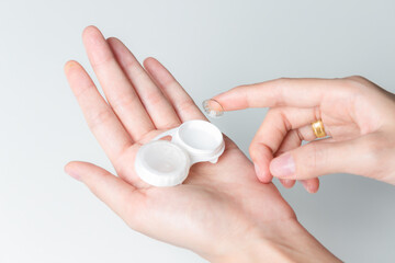 Hands of woman holding contact lenses cases and lens.