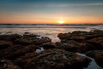 Fototapeta na wymiar Sun setting over tide pools in the Pacific Ocean. Bean Hollow State Beach, San Mateo County, California, USA.