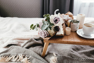Fototapeta na wymiar Coffee table on bed. Flowers, coffee cup and candles. Interior gray tones, plaid