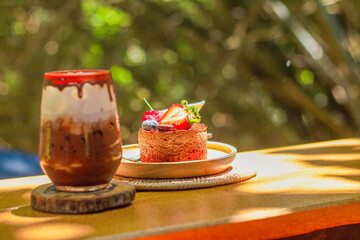 Chocolate Hazelnut Cake decorated with strawberry, raspberry, Blueberry,  and chocolate sauce, Iced chocolate - A glass of dark cocoa mixed with fresh milkand chocolate sauce on wooden table and blurr