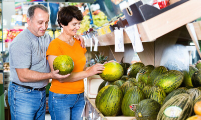 Fototapeta premium Adult cheerful male and female are choosing green melons in the store.