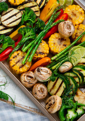 Grilled assorted vegetables in beige tray on light grey background.