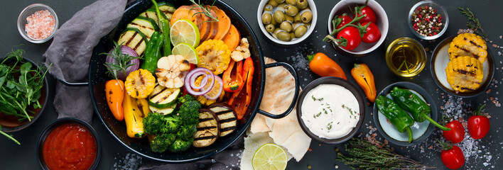 Grilled assorted vegetables in cast iron pan on black background.