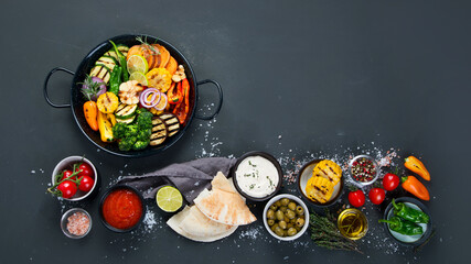 Grilled assorted vegetables in cast iron pan on black background.