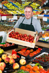 Adult man seller is demonstraiting fresh red tomatos in the store