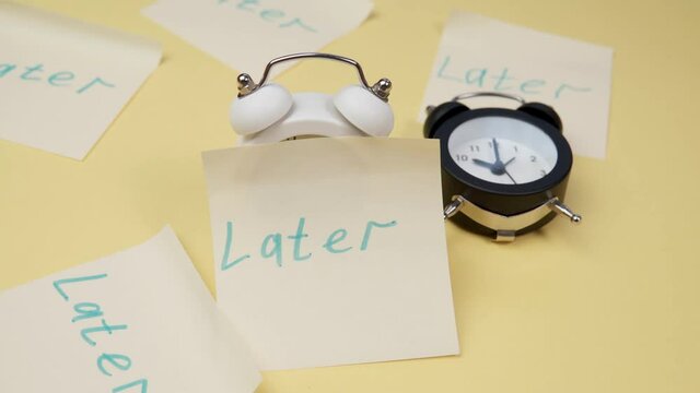 Alarm clock with a sticky note with text later. Procrastination, delay and urgency concept.