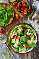 Italian pasta salad with strawberries, arugula, nuts, soft cheese dressed with balsamic sauce on the wooden table. Top view flat lay.