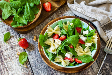 Italian pasta salad with strawberries, arugula, nuts, soft cheese dressed with balsamic sauce on the wooden table.