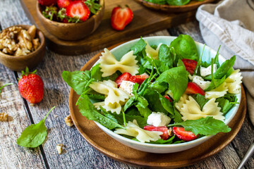 Italian pasta salad with strawberries, arugula, nuts, soft cheese dressed with balsamic sauce on the wooden table.