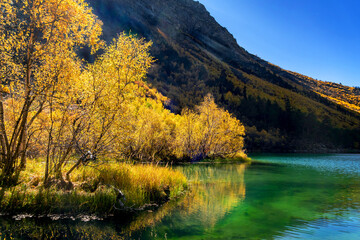 Fototapeta na wymiar Beautiful autumn landscape with clear green water of a mountain lake and reflected trees with autumn foliage and mountain peaks