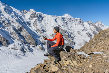 A beautiful landscape with mountains, a huge blue glacier and a middle-aged mountaineer sitting with a walkie-talkie in his hands calls the rescue service waiting for an ambulance helicopter