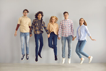 Full length group portrait of cheerful jumping young people. Full body studio shot of happy school students, college mates, or university friends in casual wear leaping for joy and having fun together
