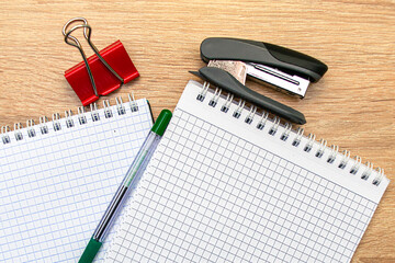 two notepads a paper clip a stapler and a fountain pen are on the table