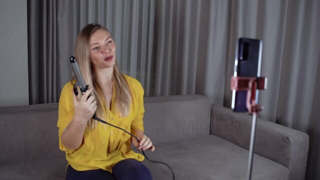Professional hairstyle. Joyful lovely woman using a professional curling iron to make a new hairstyle. Records a video blog on the phone.