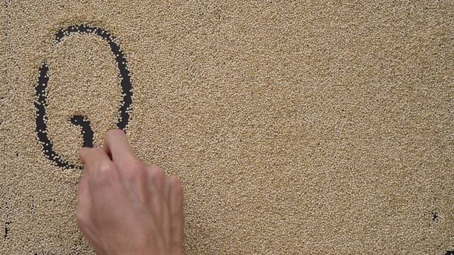 A man writes text on a black background using quinoa seeds. He writes text Quinoa