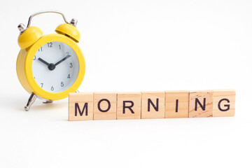 Yellow alarm clock with bell and morning text from wooden cubes