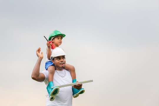 Cheerful african american father and son in hard hat, Happy dad carrying son on shoulders