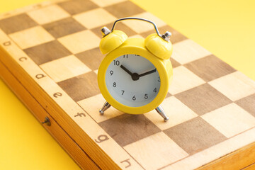 Yellow alarm clock on chess board