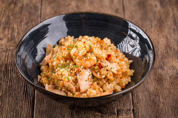 Asian seafood fried rice in a black bowl on the wooden table