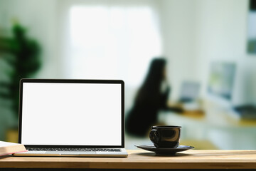 Front view of laptop computer with empty screen and coffee cup on wooden table at home office.