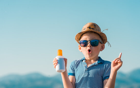Portrait of smiling little kid boy at tropical beach applying sunblock cream. Child in sunglasses and hat on sunny day. Protection from sunlight. Funny face