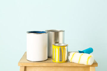 Cans of paints and roller on table against color wall