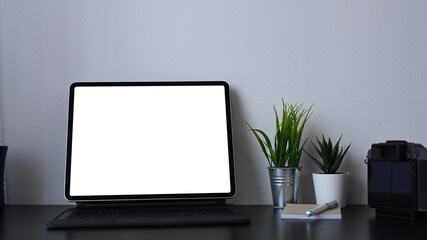 Computer tablet with empty screen, house plant and note book on modern office desk.