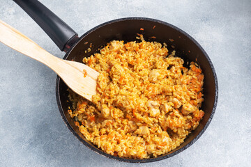 Delicious Asian pilaf, stewed rice with vegetables and chicken in a frying pan. gray concrete background. copy space.