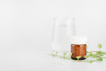 Herbal pills in glass bottle and green plant with glass of water on white background. alternative medicine and healthy lifestyle concept. copy space