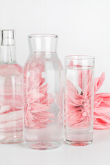 pink flowers distorted through water in glasses and bottle on white background. Home decor, eco friendly, relax, gardening concept.