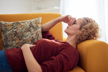 Woman with sinus pain, headache and stomach problems, lying on a couch at home.