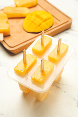 Container with homemade mango ice-cream on light background