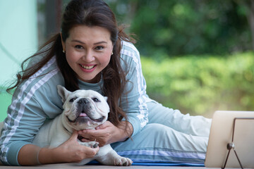 Middle-aged Asian woman relaxes with her dog after an exercise class on a tablet computer, looking at camera concept of sports and mental health