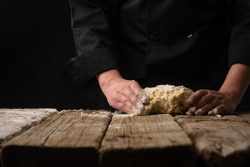 Cooking dough with the hands of a chef for homemade bread, pizza, pasta recipe.On a black background for design, with space for design.Horizontal photo, cooking and gastronomy