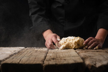 Cooking dough with the hands of a chef for homemade bread, pizza, pasta recipe.On a black background for design, with space for design.Horizontal photo, cooking and gastronomy