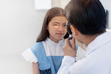 Asian optometrist examining child girl with ophthalmoscope, selective focus
