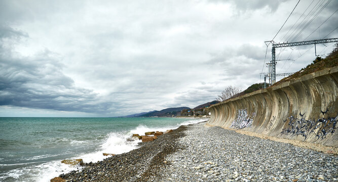 Turquoise water of the Black Sea in spring. Windy spring day. Suburban coastal landscape. Cumulus clouds float over the sea. A concrete wall painted by children protects the shore from high waves.