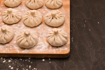 Smooth rows of raw Georgian khinkali crushed by flour lying on the corner of a kitchen board