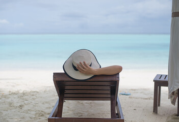 The girl wearing hat and lying down on beach chair