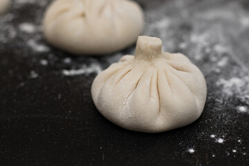 Three raw Georgian khinkali sprinkled by flour on a black table. Side view