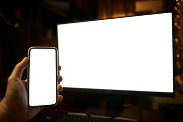 Photo of the white blank screen of the computer and hand holding cellphone. Digital web space...