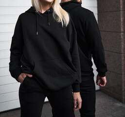 Woman stands in black no logo hoodie with bearded man behind her. Clothes branding mockup. Design...