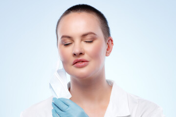 Short-haired woman doctor in medical gown taking off her mask