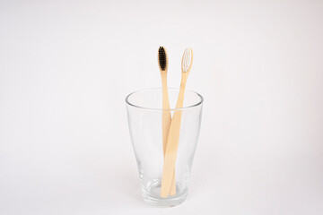 Natural wooden bamboo toothbrushes in a glass on a white background. Oral and gum care concept. Recyclable natural organic toothbrush. Flat lay, top view, copy space for text