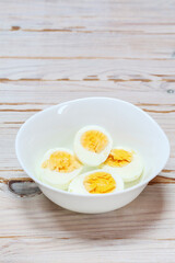 Hard-boiled eggs in a white bowl on wooden table.