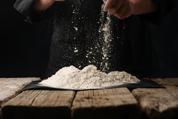 An experienced chef in a professional kitchen prepares the dough with flour to make Italian Italian pasta. concept of nature, Italy, food, diet and biology. on a dark background